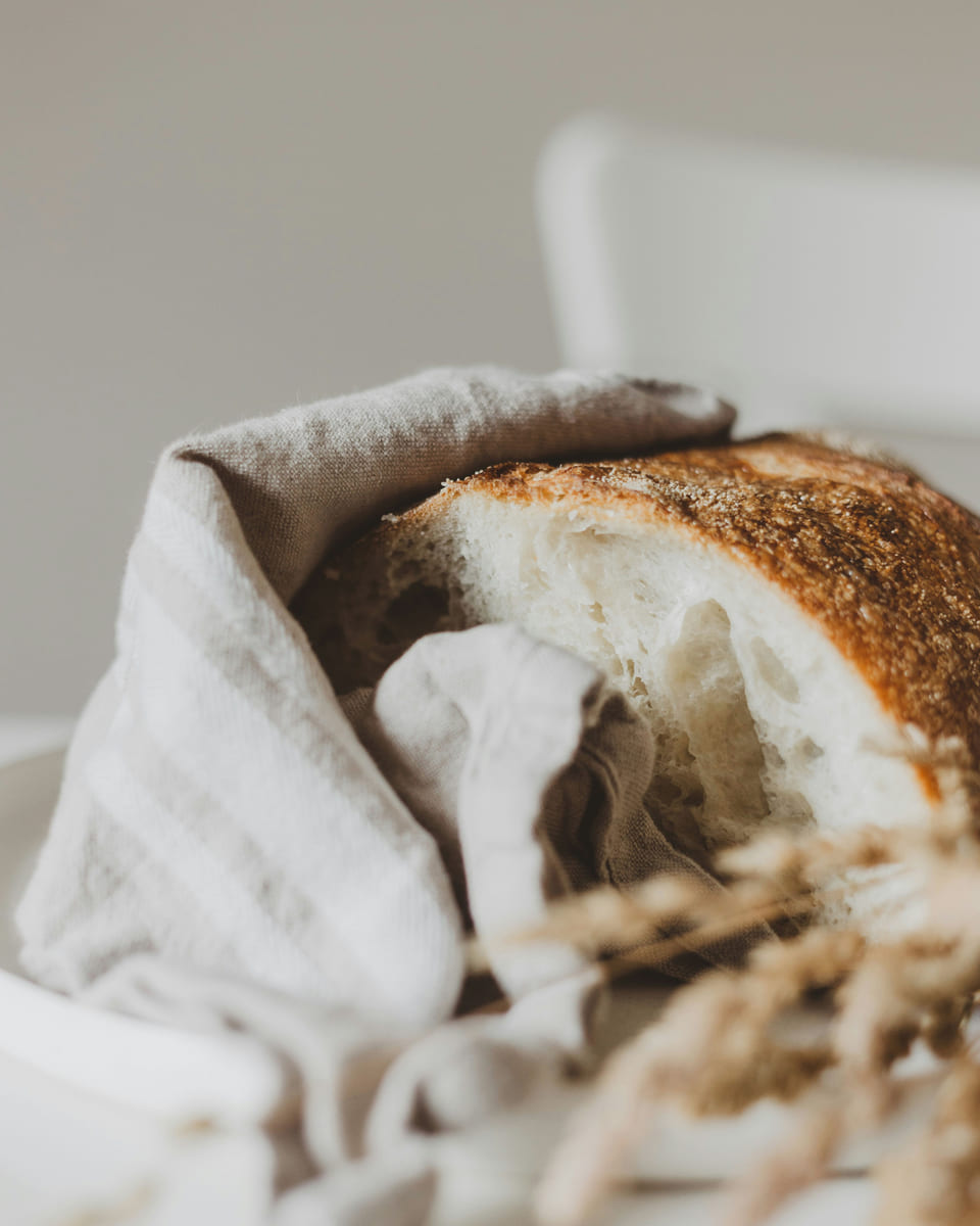 A round loaf of crusty bread wrapped in a natural linen cloth.
