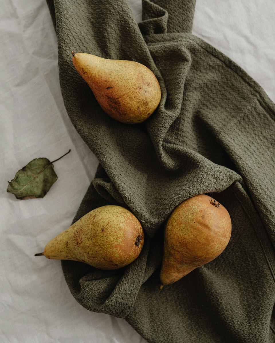 Three ripe pears resting on a folded olive-green linen cloth.
